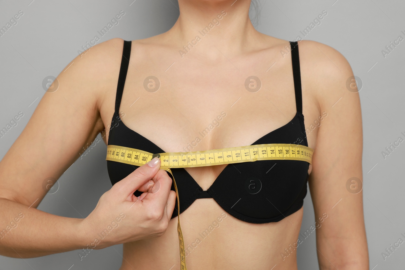 Photo of Woman in beautiful bra measuring breast circumference on light background, closeup