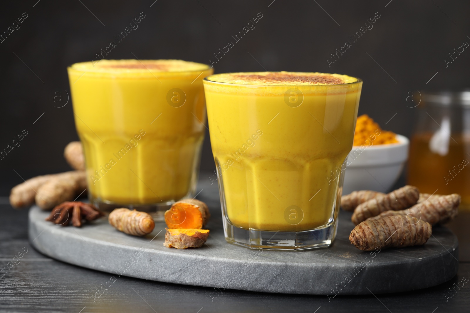 Photo of Delicious turmeric latte, powder and rhizomes on black wooden table, closeup