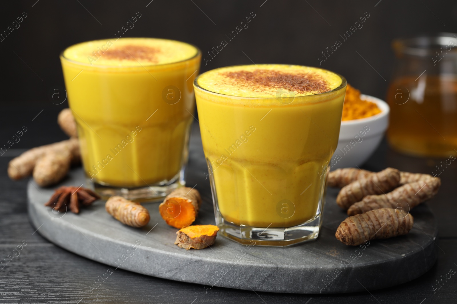 Photo of Delicious turmeric latte, powder and rhizomes on black wooden table, closeup