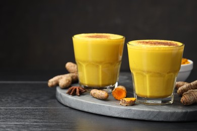 Photo of Delicious turmeric latte, powder and rhizomes on black wooden table, closeup