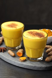 Photo of Delicious turmeric latte, powder and rhizomes on black wooden table, closeup