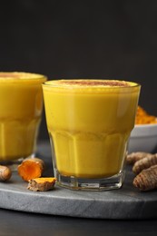 Photo of Delicious turmeric latte, powder and rhizomes on black wooden table, closeup