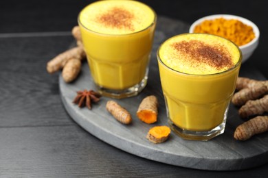 Photo of Delicious turmeric latte, powder and rhizomes on black wooden table, closeup