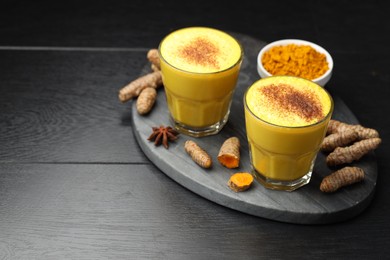 Photo of Delicious turmeric latte, powder and rhizomes on black wooden table. Space for text