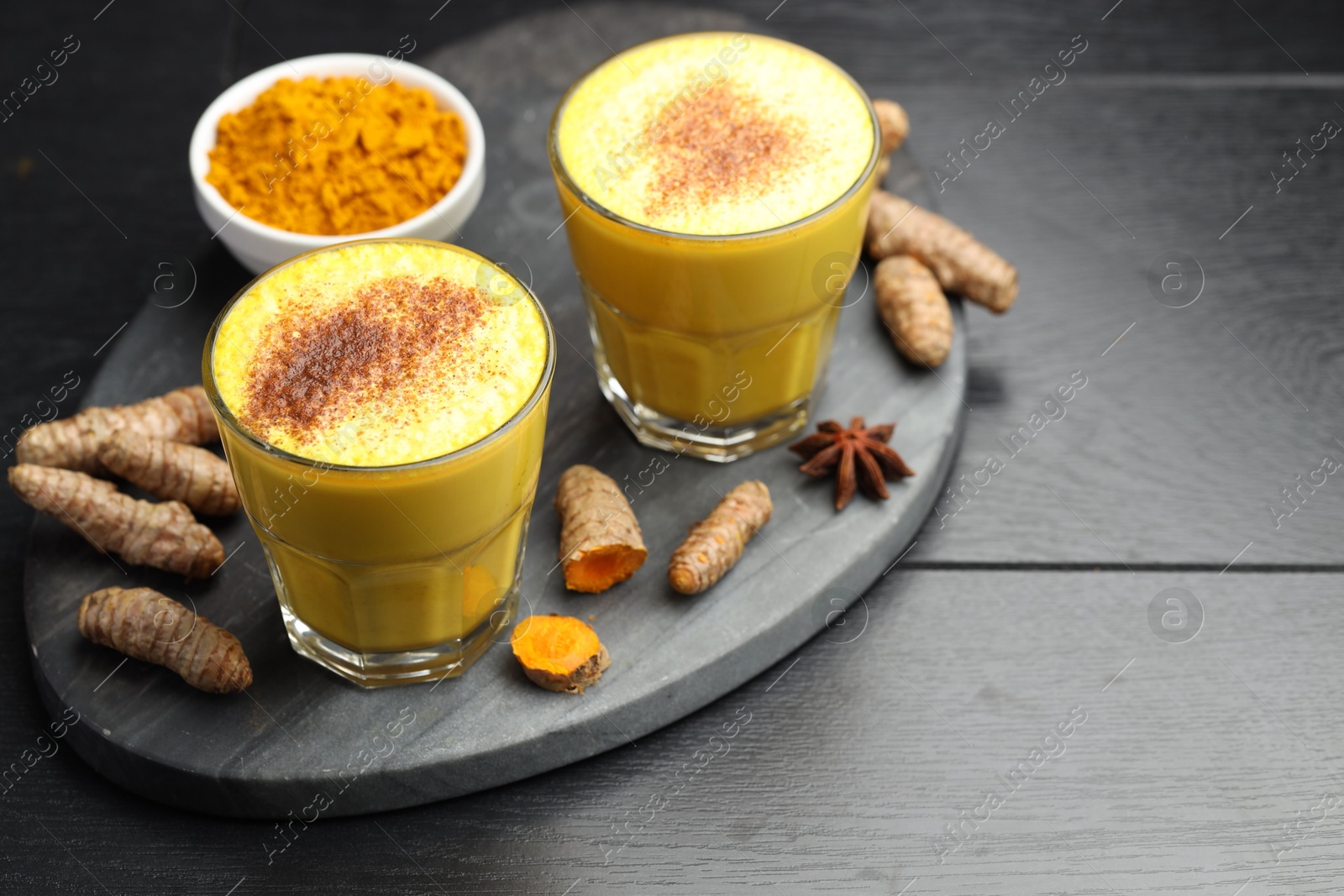 Photo of Delicious turmeric latte, powder and rhizomes on black wooden table