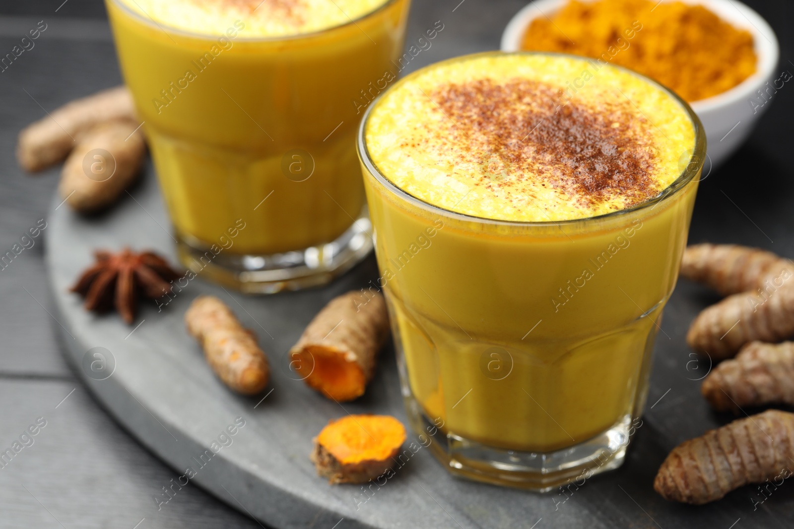 Photo of Delicious turmeric latte, powder and rhizomes on black wooden table, closeup