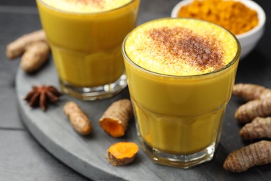 Photo of Delicious turmeric latte, powder and rhizomes on black wooden table, closeup