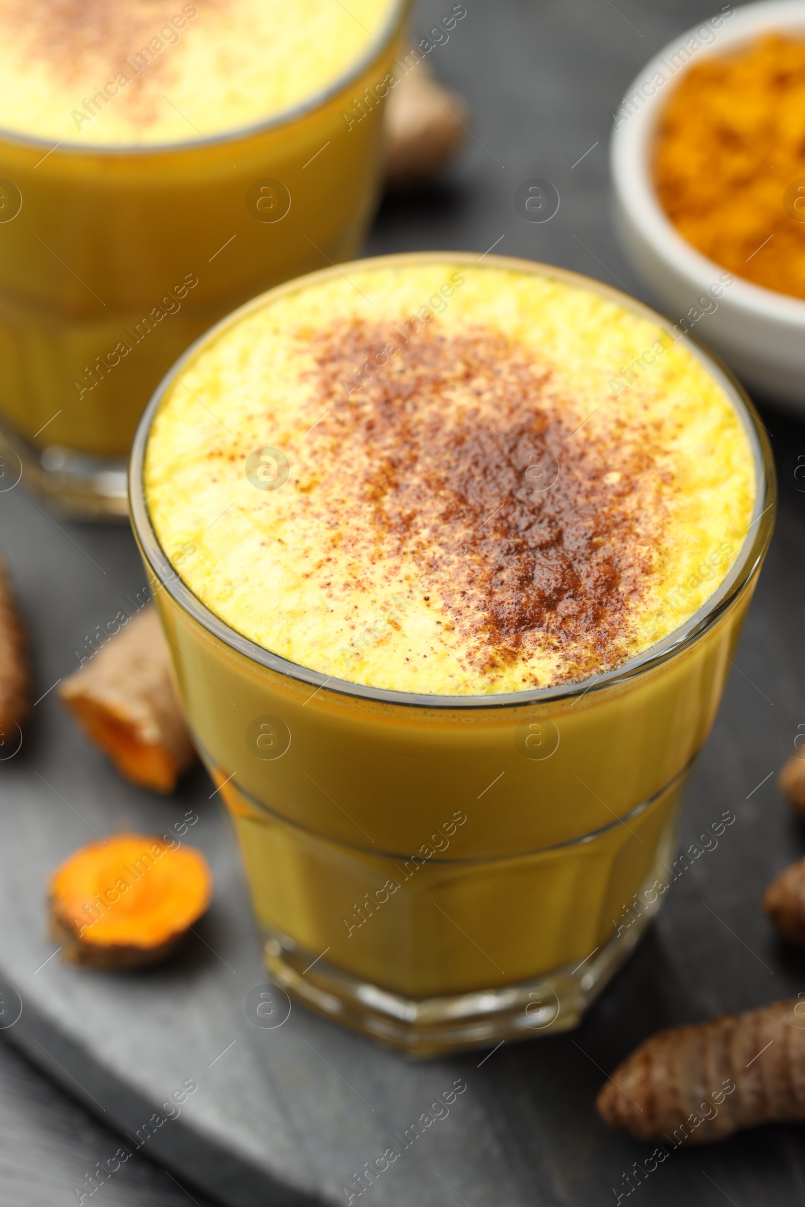 Photo of Delicious turmeric latte, powder and rhizomes on black wooden table, closeup