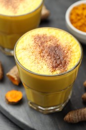 Photo of Delicious turmeric latte, powder and rhizomes on black wooden table, closeup