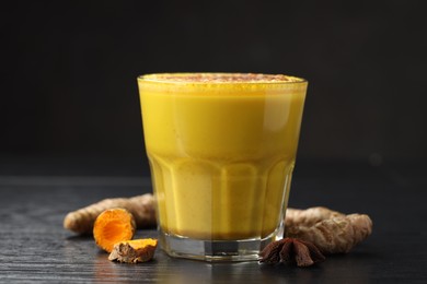 Photo of Delicious turmeric latte, powder and rhizomes on black wooden table, closeup