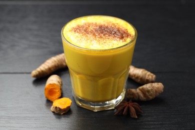 Photo of Delicious turmeric latte, powder and rhizomes on black wooden table, closeup