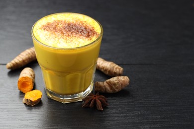 Photo of Delicious turmeric latte, powder and rhizomes on black wooden table, closeup. Space for text