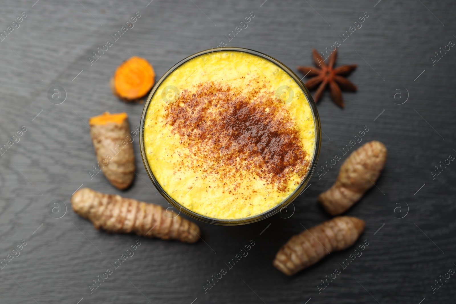 Photo of Delicious turmeric latte, powder and rhizomes on black wooden table, top view