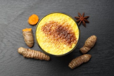 Photo of Delicious turmeric latte, powder and rhizomes on black wooden table, top view