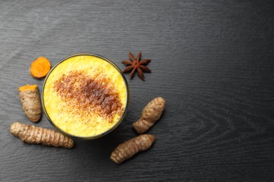 Photo of Delicious turmeric latte, powder and rhizomes on black wooden table, top view. Space for text