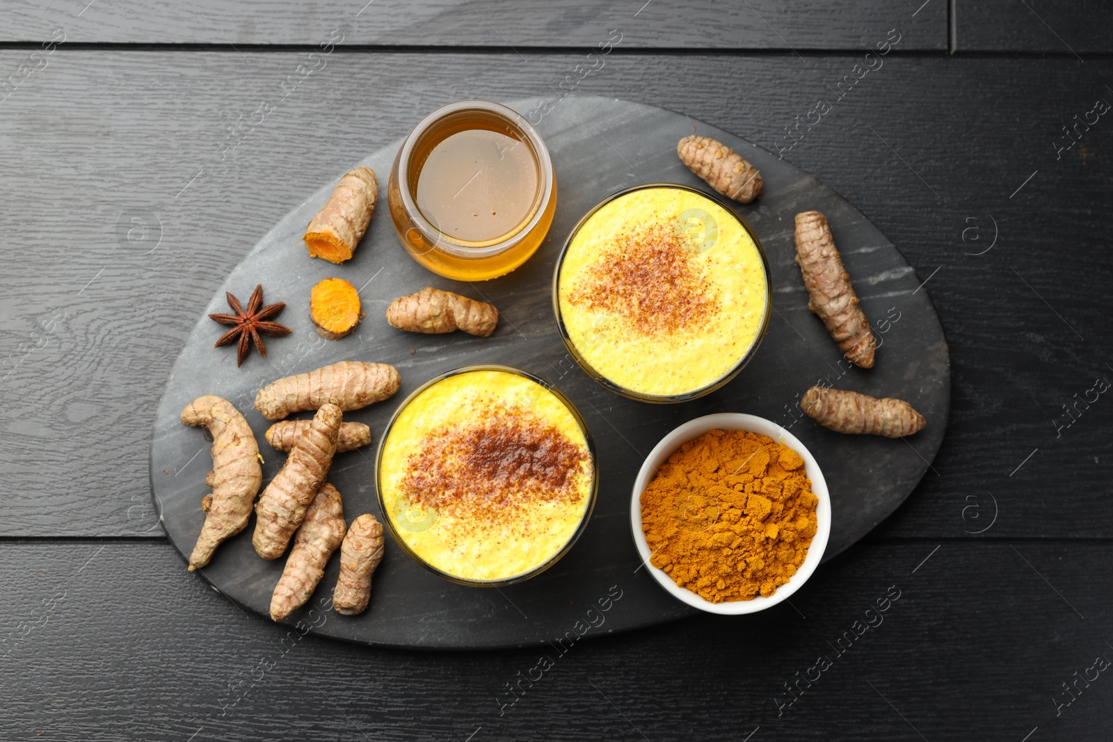 Photo of Delicious turmeric latte, powder and rhizomes on black wooden table, flat lay