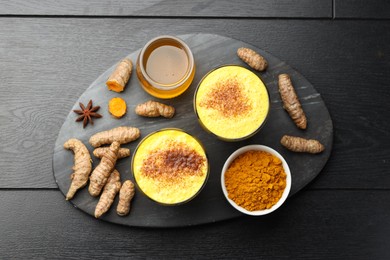 Photo of Delicious turmeric latte, powder and rhizomes on black wooden table, flat lay