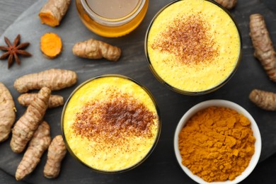 Delicious turmeric latte, powder and rhizomes on black wooden table, flat lay