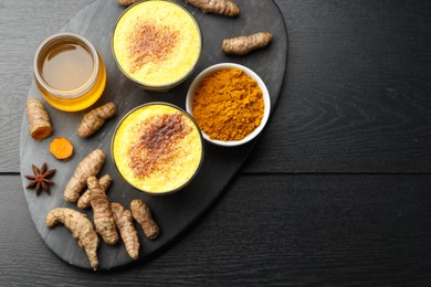 Photo of Delicious turmeric latte, powder and rhizomes on black wooden table, flat lay