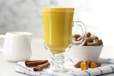 Photo of Delicious turmeric latte and rhizomes on white wooden table, closeup