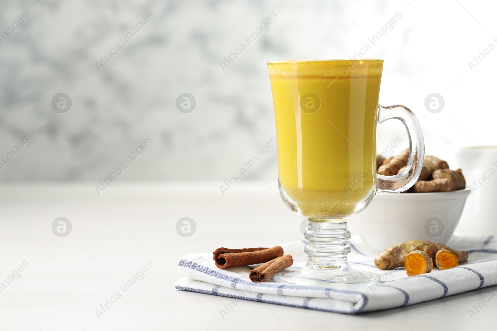 Photo of Delicious turmeric latte and rhizomes on white wooden table. Space for text