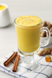 Photo of Delicious turmeric latte and rhizomes on white wooden table, closeup