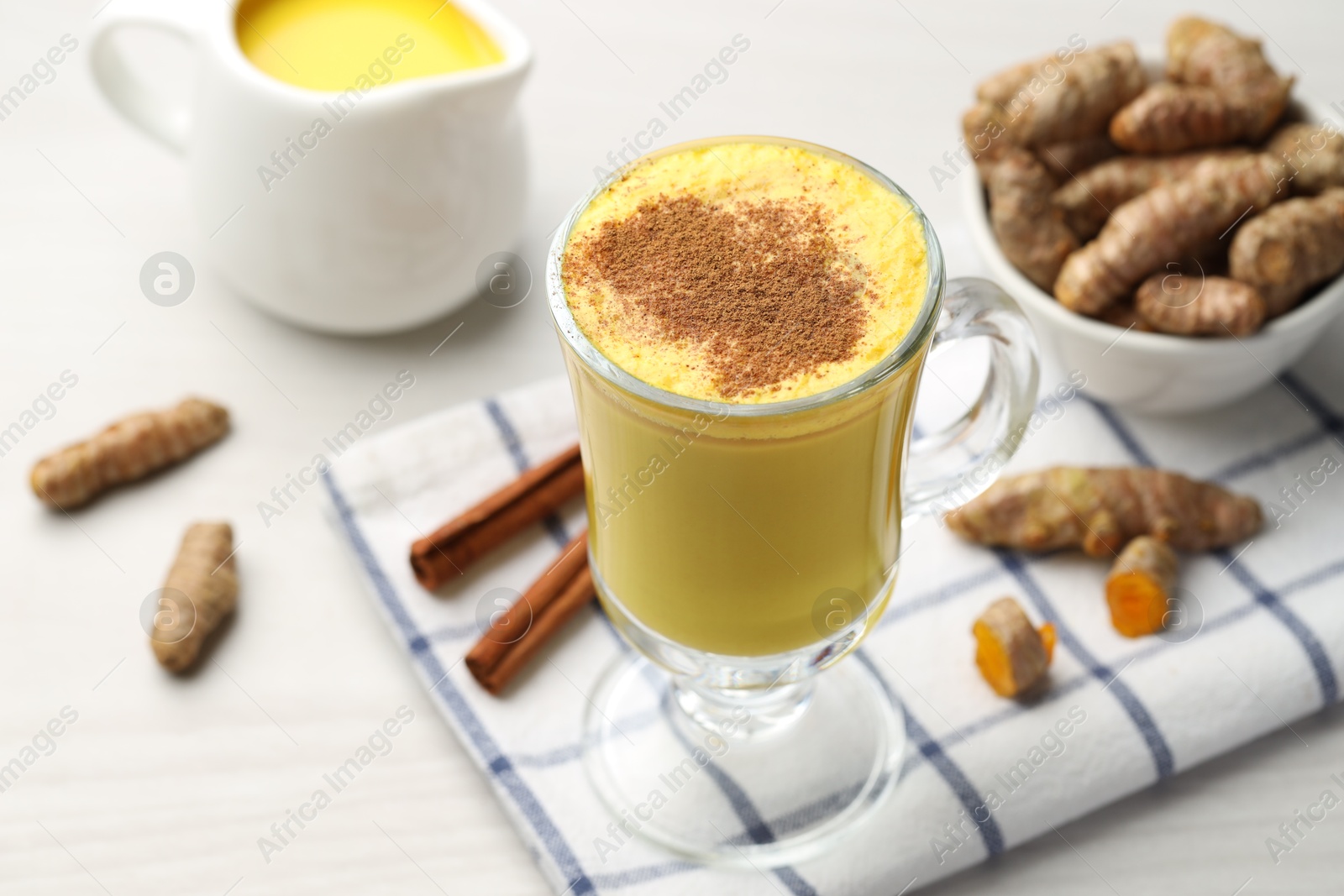 Photo of Delicious turmeric latte and rhizomes on white wooden table, closeup