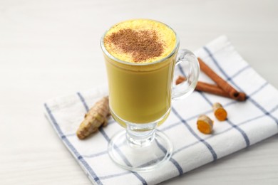 Photo of Delicious turmeric latte and rhizomes on white wooden table, closeup