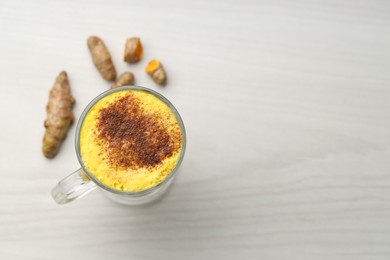 Photo of Delicious turmeric latte and rhizomes on white wooden table, flat lay. Space for text