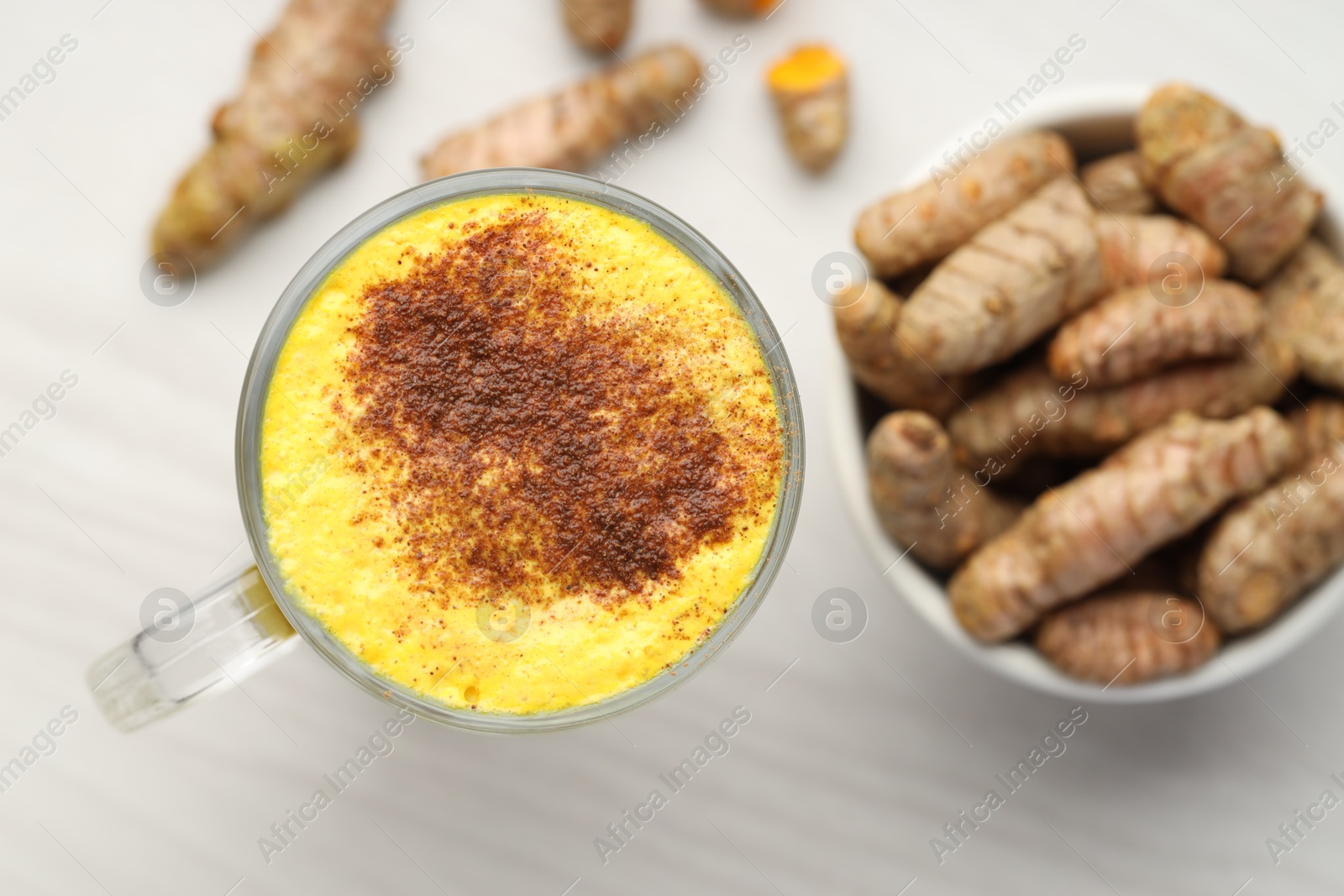 Photo of Delicious turmeric latte and rhizomes on white wooden table, flat lay