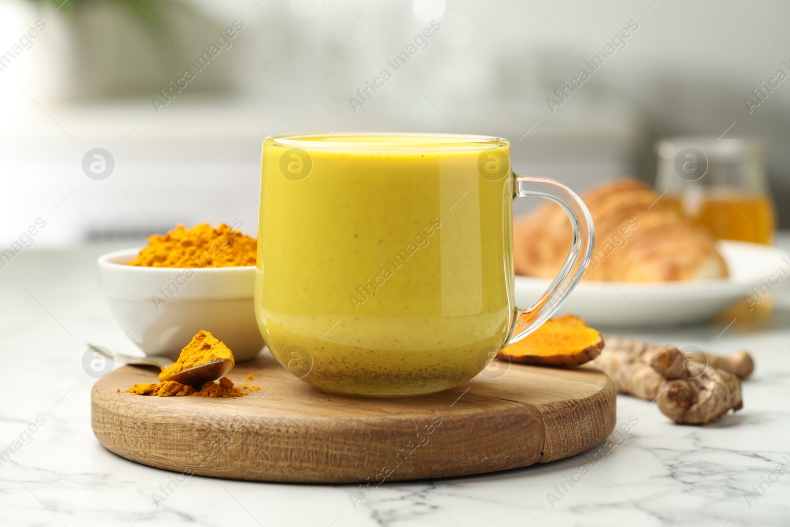 Photo of Delicious turmeric latte, powder and rhizomes on white marble table, closeup