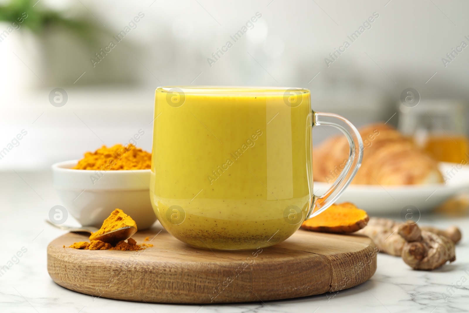 Photo of Delicious turmeric latte, powder and rhizomes on white marble table, closeup