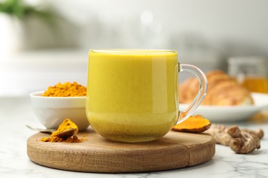 Photo of Delicious turmeric latte, powder and rhizomes on white marble table, closeup