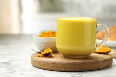 Photo of Delicious turmeric latte, powder and rhizomes on white marble table, closeup