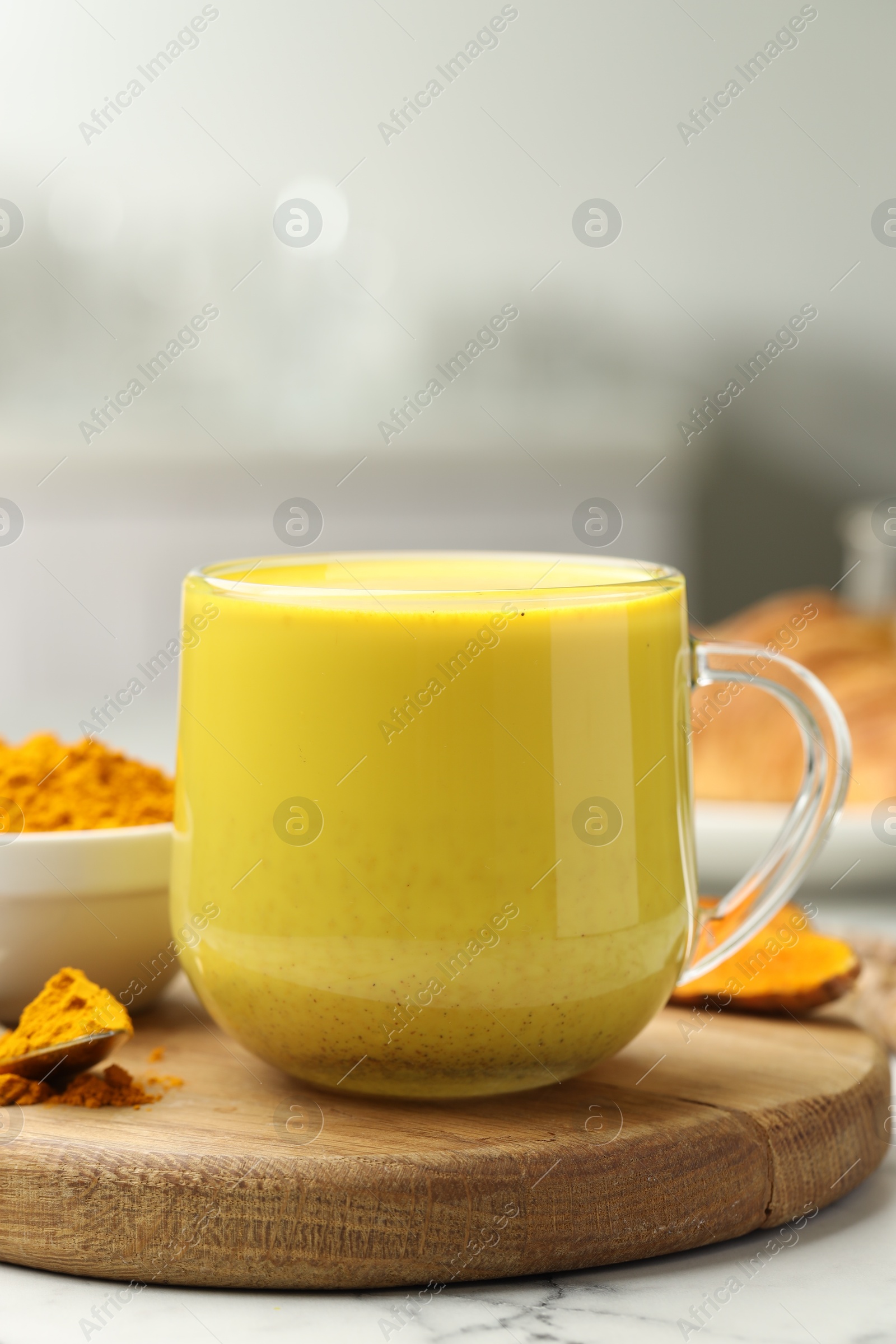 Photo of Delicious turmeric latte, powder and rhizomes on white marble table, closeup