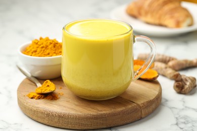 Photo of Delicious turmeric latte, powder and rhizomes on white marble table, closeup