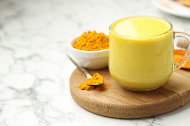 Photo of Delicious turmeric latte, powder and rhizomes on white marble table, closeup. Space for text