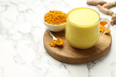 Photo of Delicious turmeric latte, powder and rhizomes on white marble table, closeup. Space for text