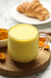 Photo of Delicious turmeric latte, powder and rhizomes on white marble table, closeup