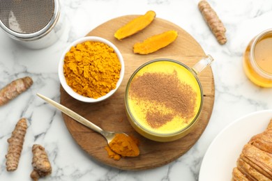 Photo of Delicious turmeric latte, powder and rhizomes on white marble table, flat lay