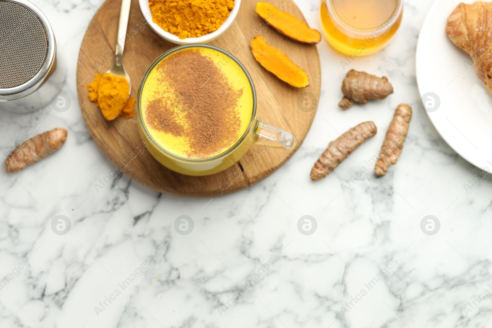 Photo of Delicious turmeric latte, powder and rhizomes on white marble table, flat lay. Space for text