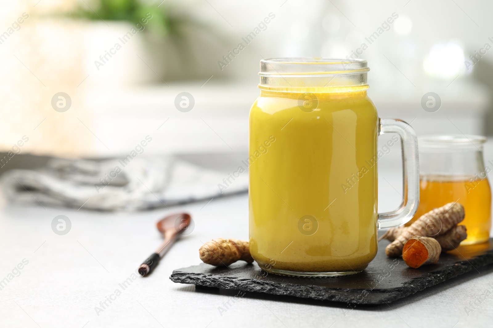 Photo of Delicious turmeric latte with honey and rhizomes on grey table, closeup. Space for text