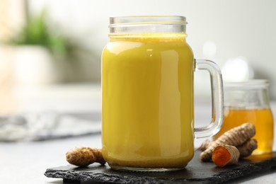 Delicious turmeric latte with honey and rhizomes on grey table, closeup