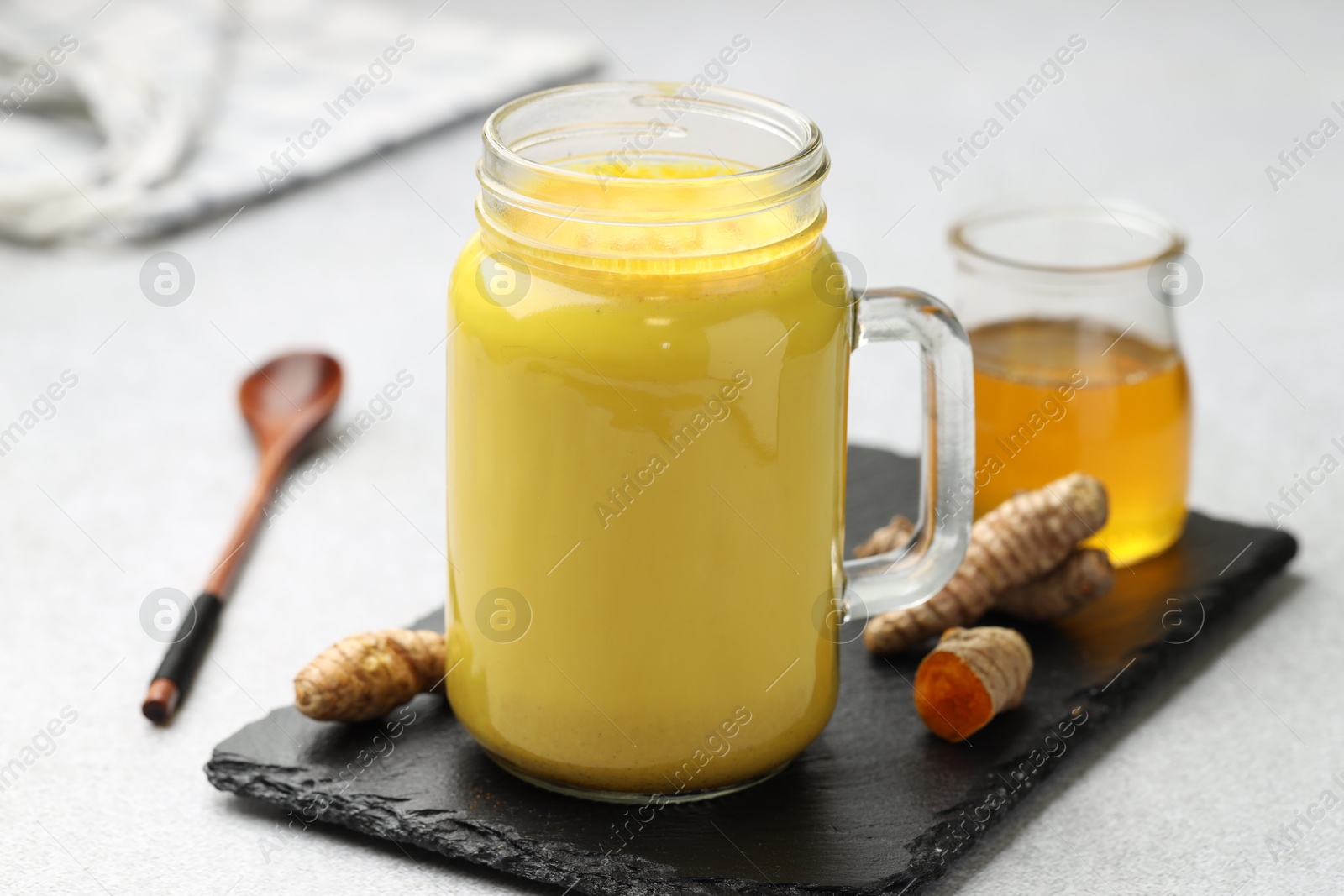 Photo of Delicious turmeric latte with honey and rhizomes on grey table, closeup