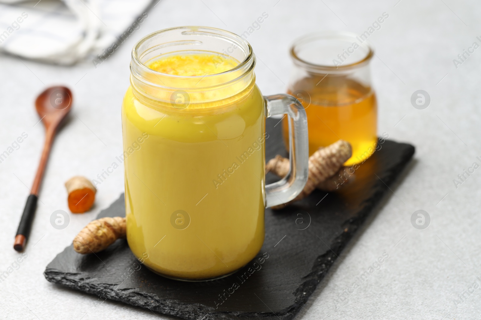 Photo of Delicious turmeric latte with honey and rhizomes on grey table, closeup