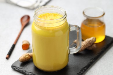 Photo of Delicious turmeric latte with honey and rhizomes on grey table, closeup