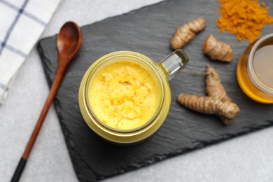 Photo of Delicious turmeric latte with honey, powder and rhizomes on grey table, flat lay