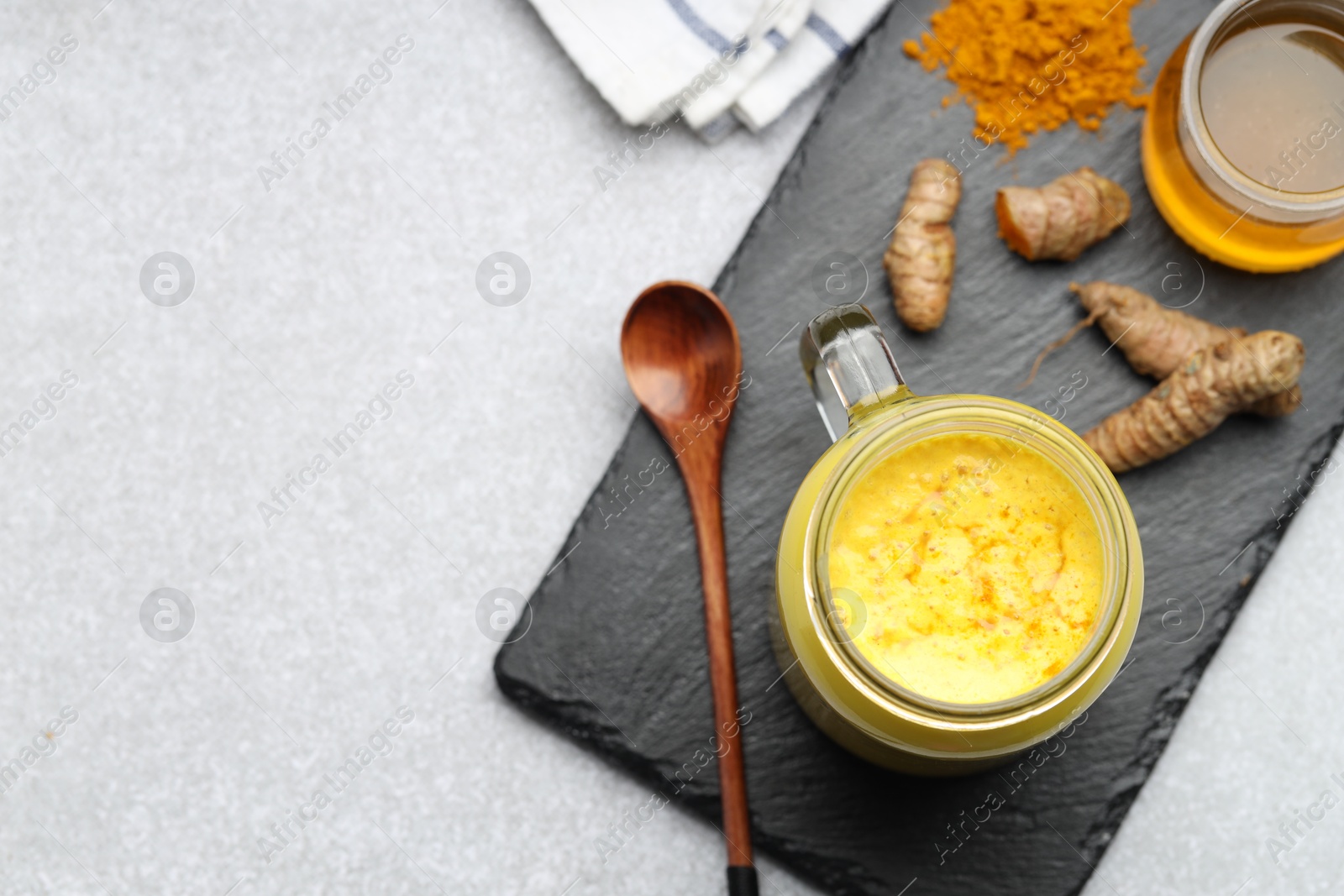 Photo of Delicious turmeric latte with honey, powder and rhizomes on grey table, flat lay. Space for text