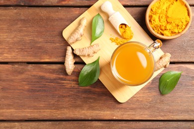 Photo of Aromatic turmeric tea in glass mug, roots, powder and leaves on wooden table, flat lay. Space for text