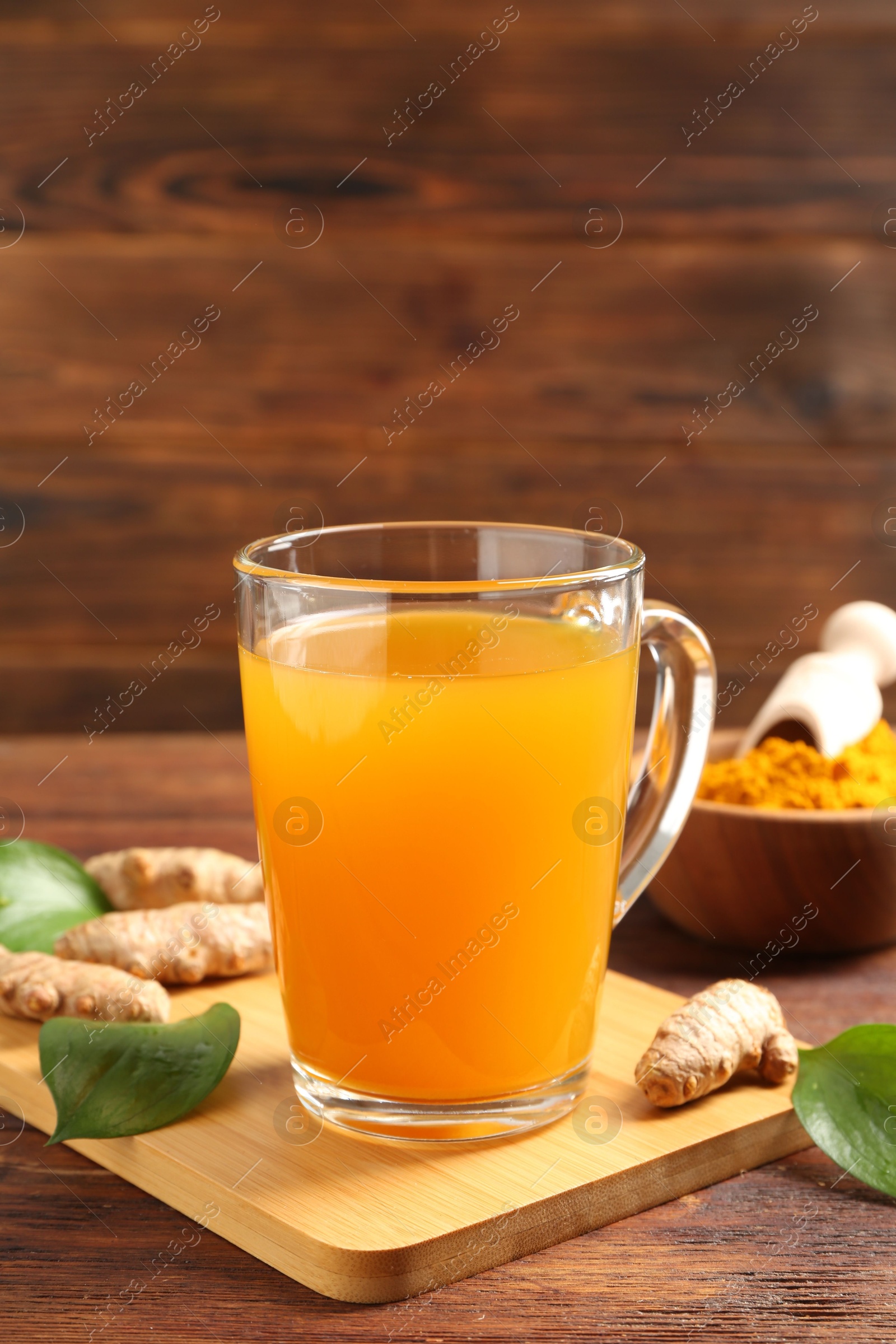 Photo of Aromatic turmeric tea in glass mug, roots, powder and green leaves on wooden table